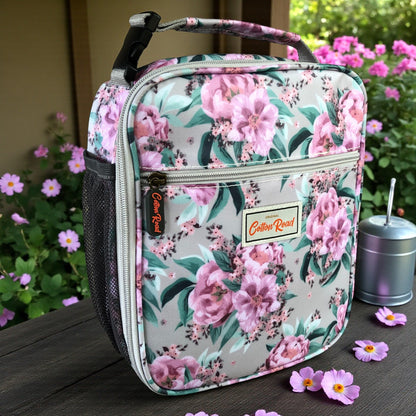 COTTON ROAD COOLER PINK Floral-patterned lunch bag standing on a wooden bench with flowers in the background 