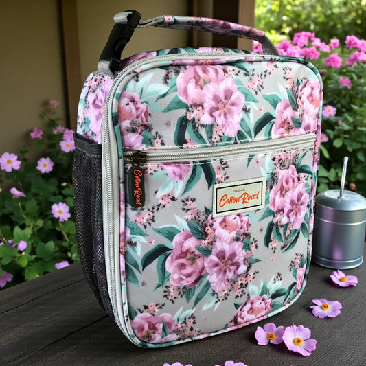 COTTON ROAD COOLER PINK Floral-patterned lunch bag standing on a wooden bench with flowers in the background 
