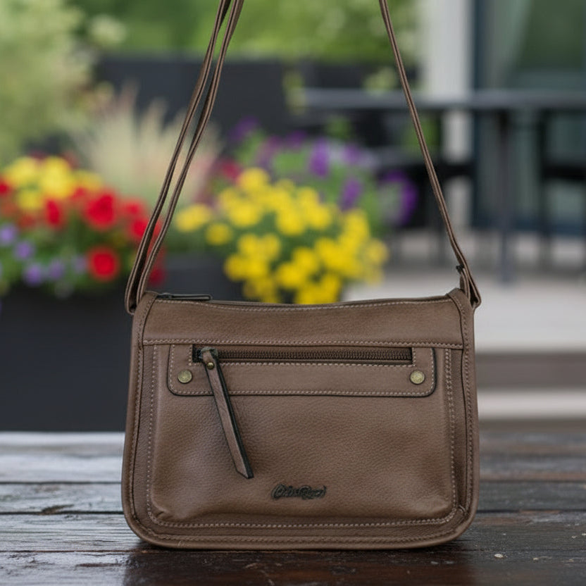 Cotton Road Khaki PU Leather Sling Bag on sleeper table and blurred patio background with red and yellow flowers