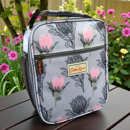 COTTON ROAD COOLER BLUE PROTEA patterned lunch bag on a wooden bench with flowers in the background