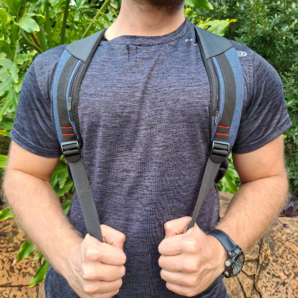 Person wearing/ carrying a blue and black Vivace backpack to show the view from the front over the shoulders straps with greenery in the background
