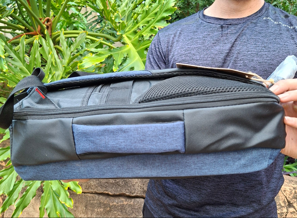 Person holding a black and blue Vivace travel backpack outdoors with greenery in the background