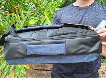 Person holding a black and blue Vivace travel backpack outdoors with greenery in the background