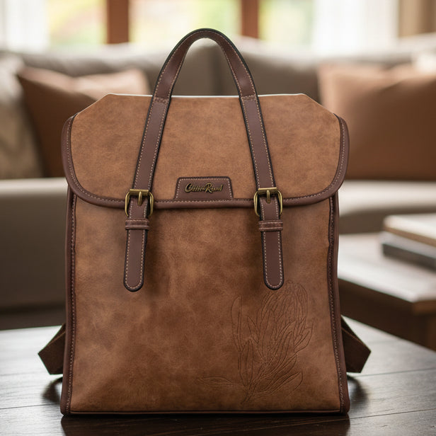 Brown Cotton Road PU leather backpack with embossed protea design on a table and blurred living room background