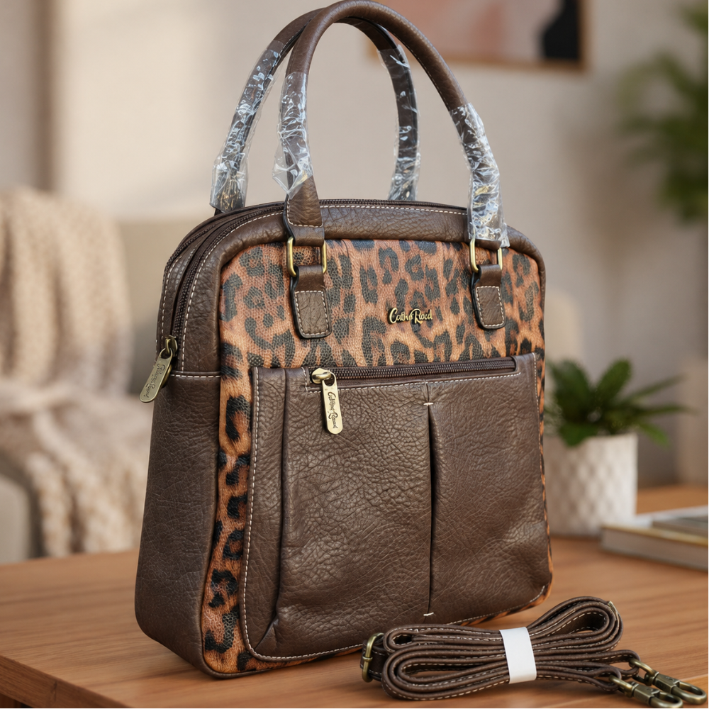 Cotton Road dark brown PU leather handbag with leopard print panels and detachable shoulder strap displayed on a wooden table in a modern indoor lifestyle setting.